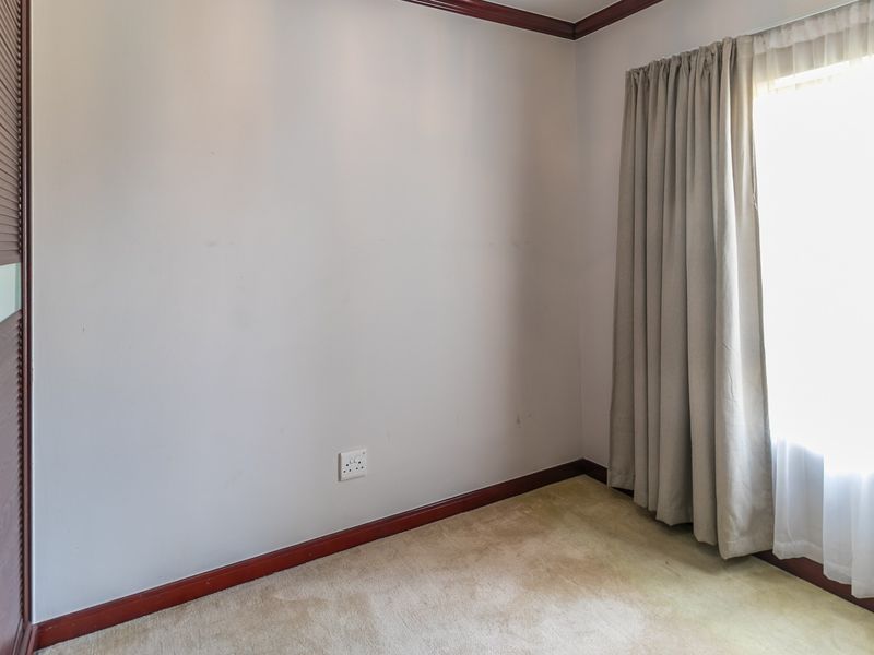 An empty bedroom featuring built-in wardrobe storage, carpeted flooring, and neutral wall finishes with natural light from the window.
