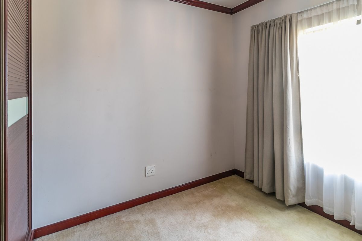 An empty bedroom featuring built-in wardrobe storage, carpeted flooring, and neutral wall finishes with natural light from the window.