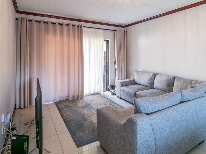 A bright living room featuring tiled flooring, crown molding, and a sliding glass door providing access to the outdoor area.