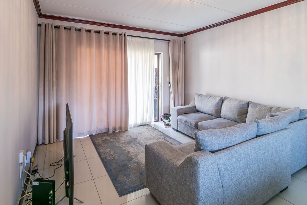 A bright living room featuring tiled flooring, crown molding, and a sliding glass door providing access to the outdoor area.