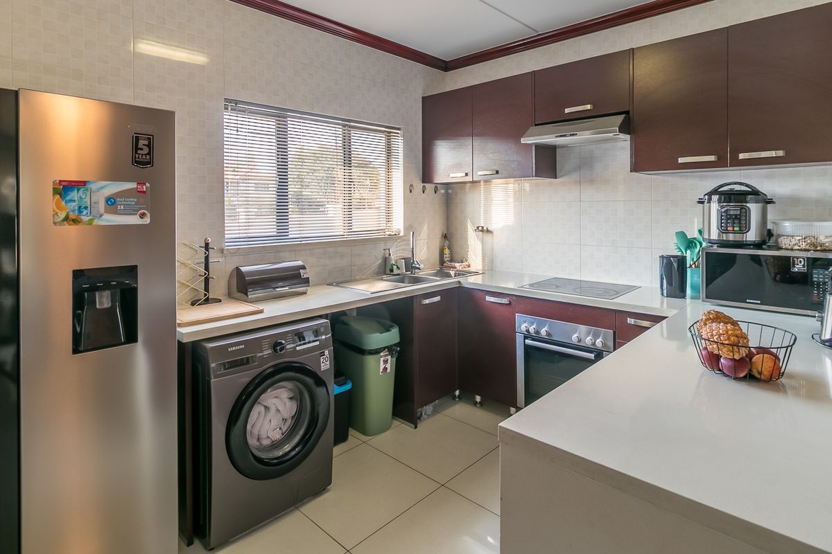 A functional kitchen featuring dark wood cabinetry, stone countertops, integrated appliances, and tiled finishes, offering a clean and practical workspace.