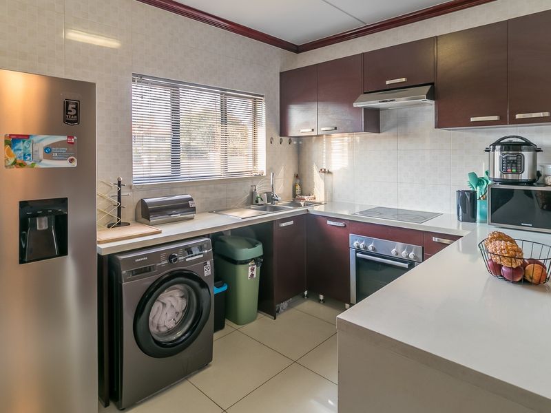 A functional kitchen featuring dark wood cabinetry, stone countertops, integrated appliances, and tiled finishes, offering a clean and practical workspace.