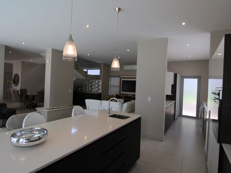 Modern open-plan living area featuring a sleek kitchen island with quartz countertops, integrated cabinetry, and tiled flooring, flowing into the lounge and dining space.
