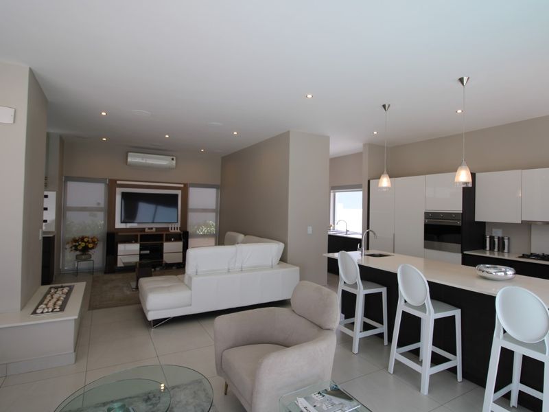 Modern open-plan living area featuring a sleek kitchen with island, built-in appliances, and tiled flooring, seamlessly flowing into the lounge space.