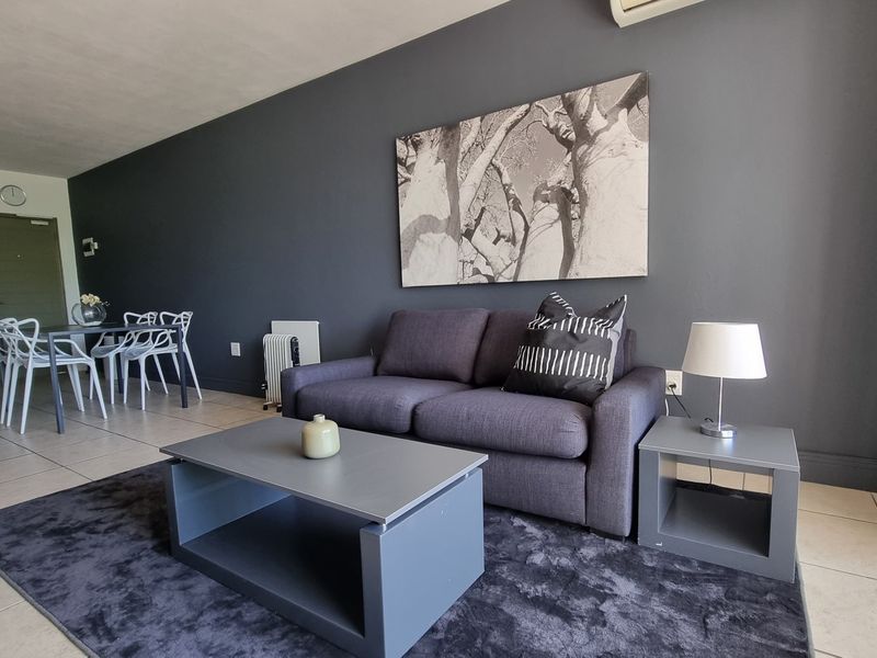 An open-plan living and dining area featuring tiled floors, a dark accent wall, and an integrated kitchen space.