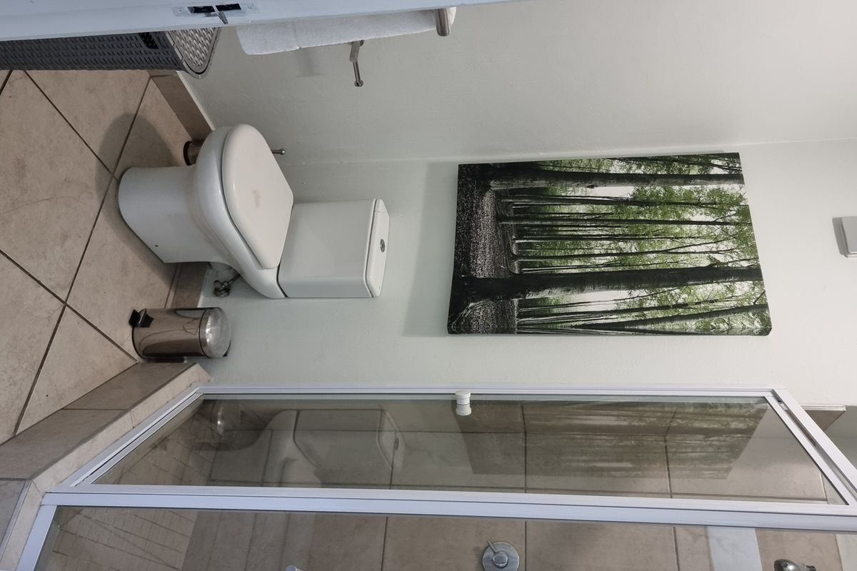 A functional bathroom featuring a glass-enclosed shower, tiled flooring, and a standard toilet, finished with neutral wall tones.