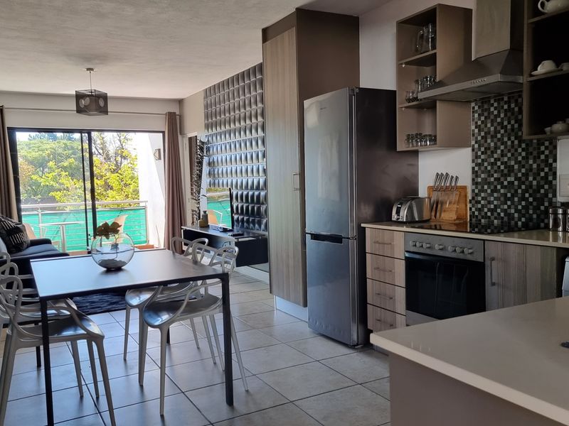 Open-plan living and kitchen area featuring tiled floors, modern cabinetry, integrated appliances, and a sliding door leading to a balcony.