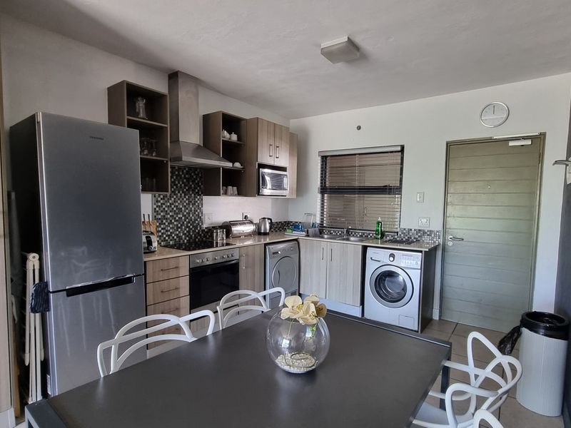 Open-plan kitchen and dining area featuring modern cabinetry, built-in appliances, tiled backsplash, and direct access to the apartment entrance.