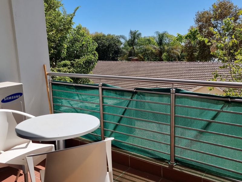 A balcony featuring tiled flooring, a stainless steel railing, and an external air conditioning unit, offering an elevated view of the surrounding neighborhood.