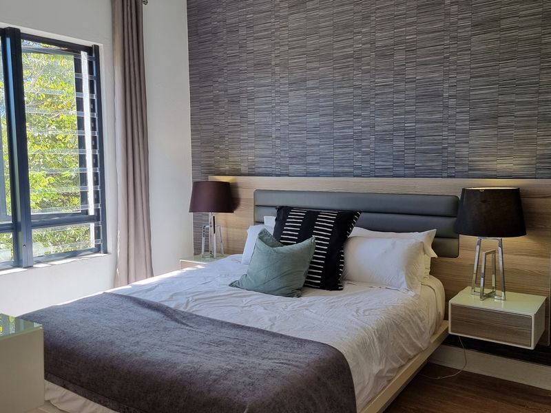 A well-maintained bedroom featuring a modern built-in headboard with integrated floating bedside tables and large louvered windows providing natural light.