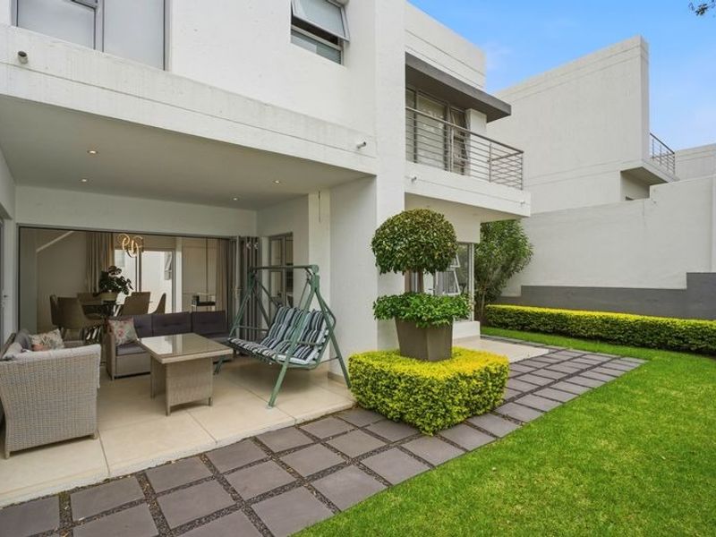 A well-maintained covered patio area featuring tiled flooring and recessed lighting, seamlessly connecting to a private garden with a paved walkway.