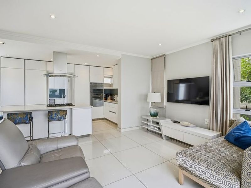 Modern open-plan living area featuring a sleek kitchen with built-in appliances, high-gloss cabinetry, and polished porcelain floor tiles throughout.
