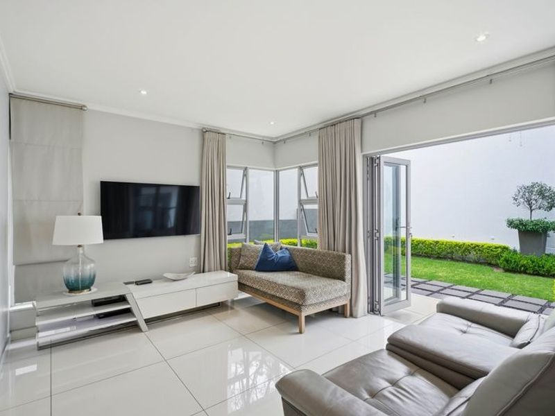 Bright and modern living room featuring large porcelain floor tiles, recessed lighting, and seamless aluminium stacker doors opening onto a private garden.