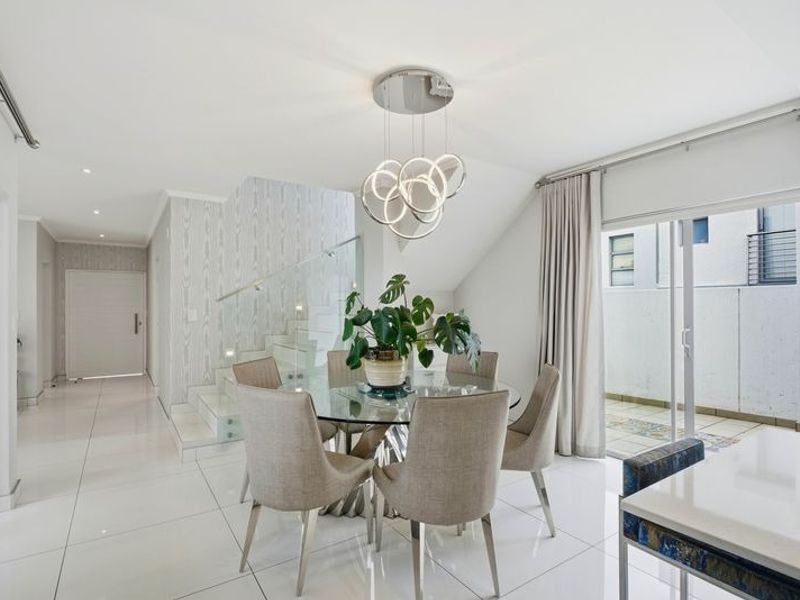 Bright open-plan dining area featuring sleek porcelain floor tiles, a modern glass staircase balustrade, and direct access to an outdoor patio through sliding doors.