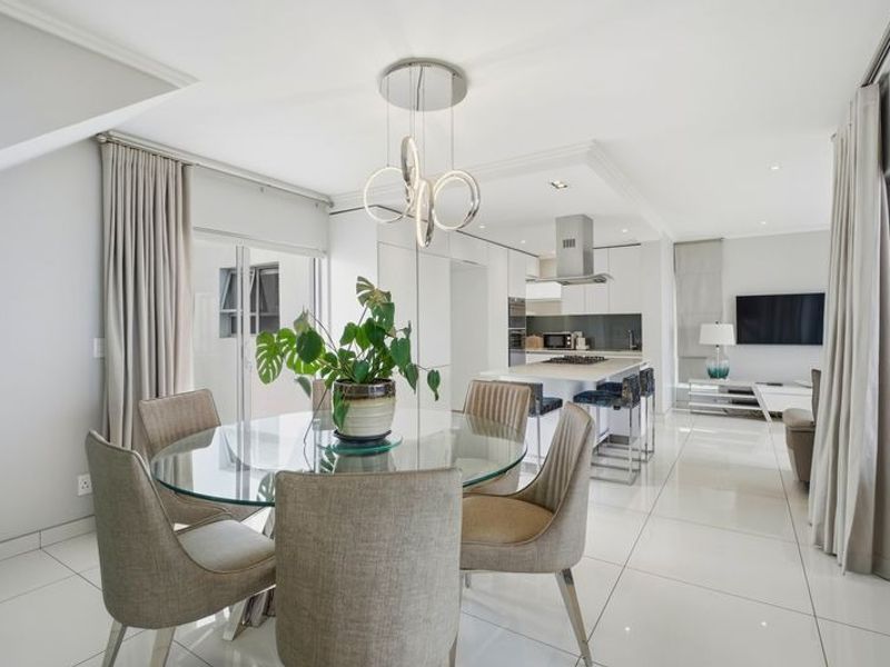 Modern open-plan living area featuring a sleek kitchen with island, high-gloss cabinetry, integrated appliances, and bright tiled flooring leading to a dining space.