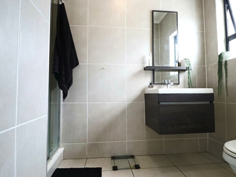 A modern bathroom featuring a wall-mounted vanity with an integrated basin, a shower enclosure, and neutral wall and floor tiling.