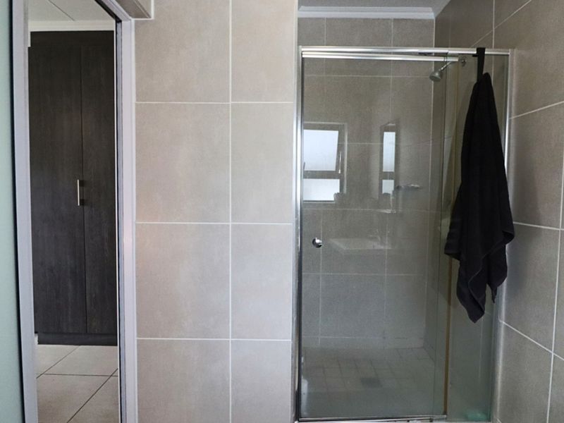 A functional bathroom featuring a glass-enclosed shower with neutral wall tiling and an adjacent built-in storage cupboard.