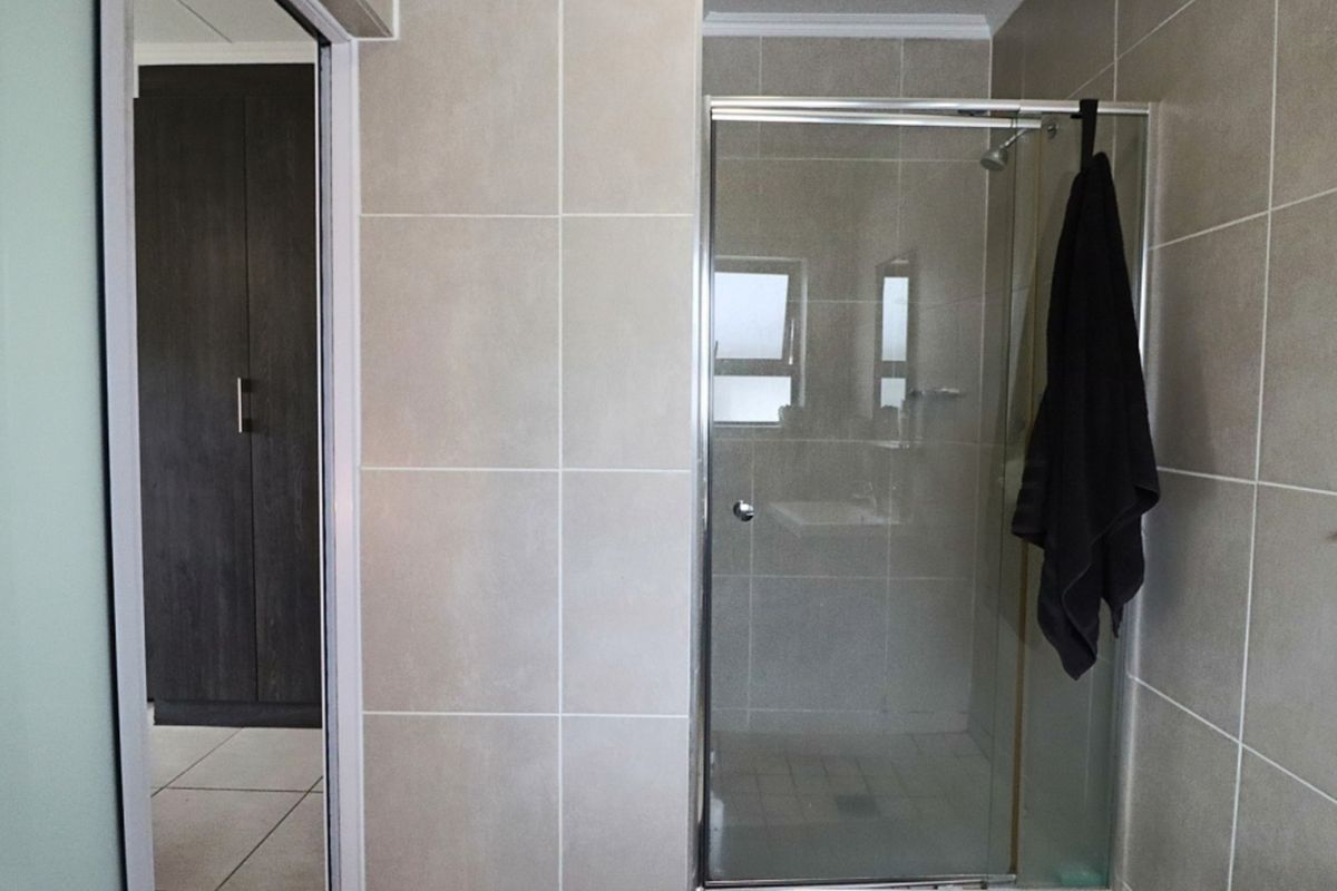 A functional bathroom featuring a glass-enclosed shower with neutral wall tiling and an adjacent built-in storage cupboard.