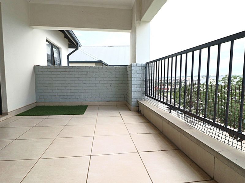 A spacious covered balcony featuring tiled flooring, a painted brick feature wall, and a secure metal balustrade with views.
