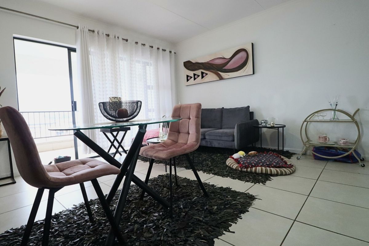 A bright living area featuring neutral tiled flooring and a sliding glass door providing direct access to an outdoor balcony space.