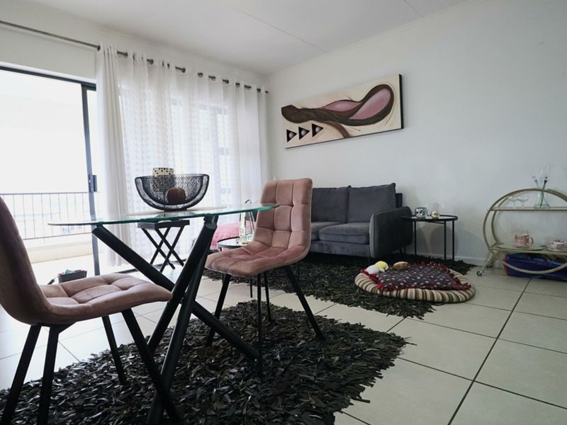 A bright living area featuring neutral tiled flooring and a sliding glass door providing direct access to an outdoor balcony space.