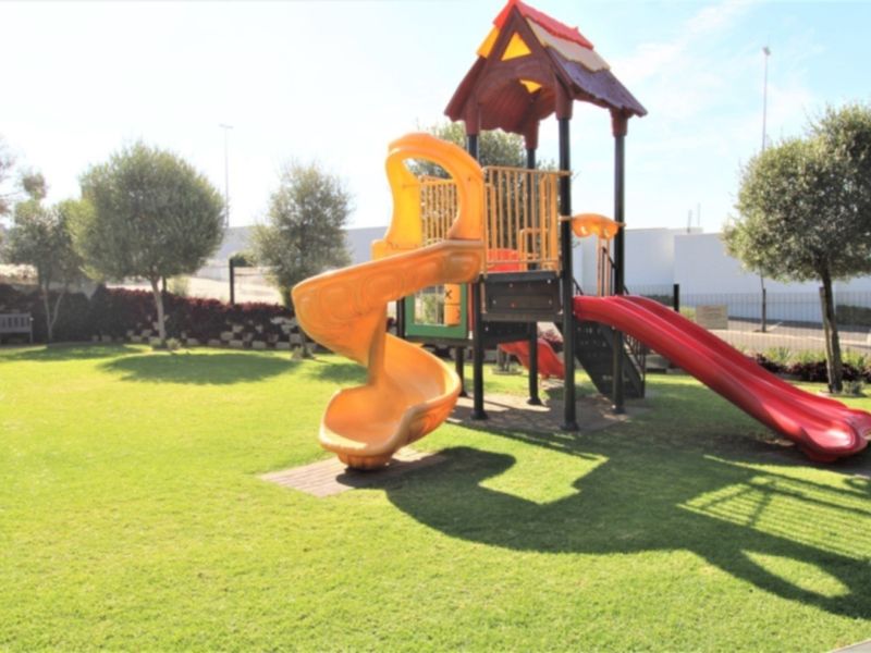 A well-maintained communal garden area featuring a children's playground set on a manicured lawn with perimeter fencing.