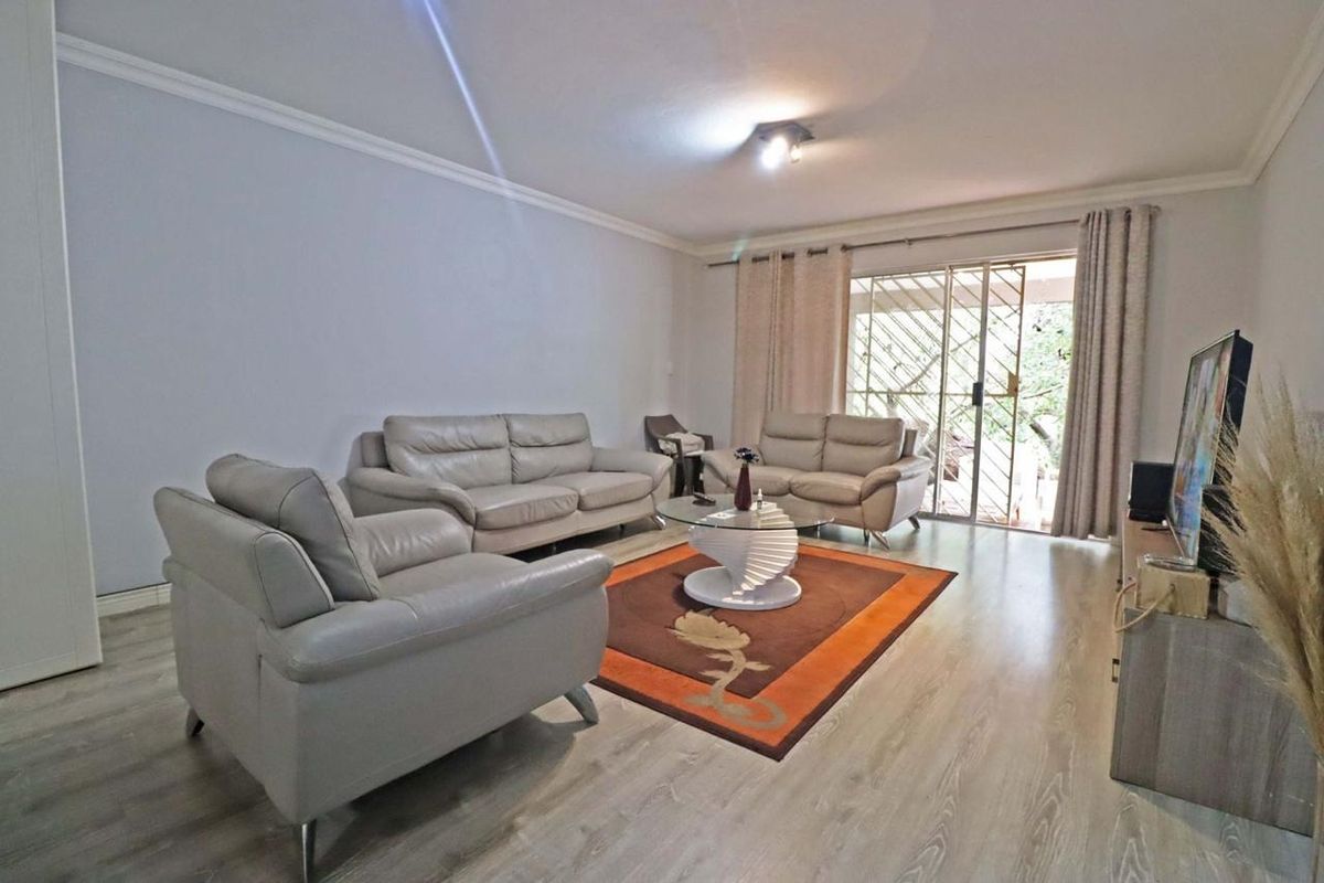 A well-maintained living room featuring laminate flooring, coving, and a sliding glass door with an integrated security gate leading to the exterior.