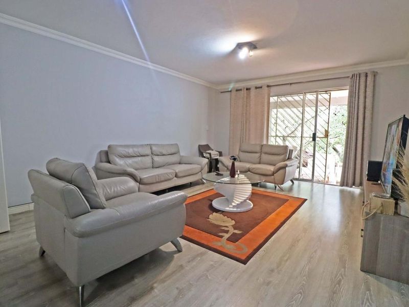 A well-maintained living room featuring laminate flooring, coving, and a sliding glass door with an integrated security gate leading to the exterior.