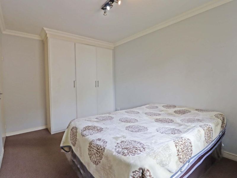 A simple bedroom featuring neutral walls, carpeted flooring, crown molding, and a built-in wardrobe for storage.