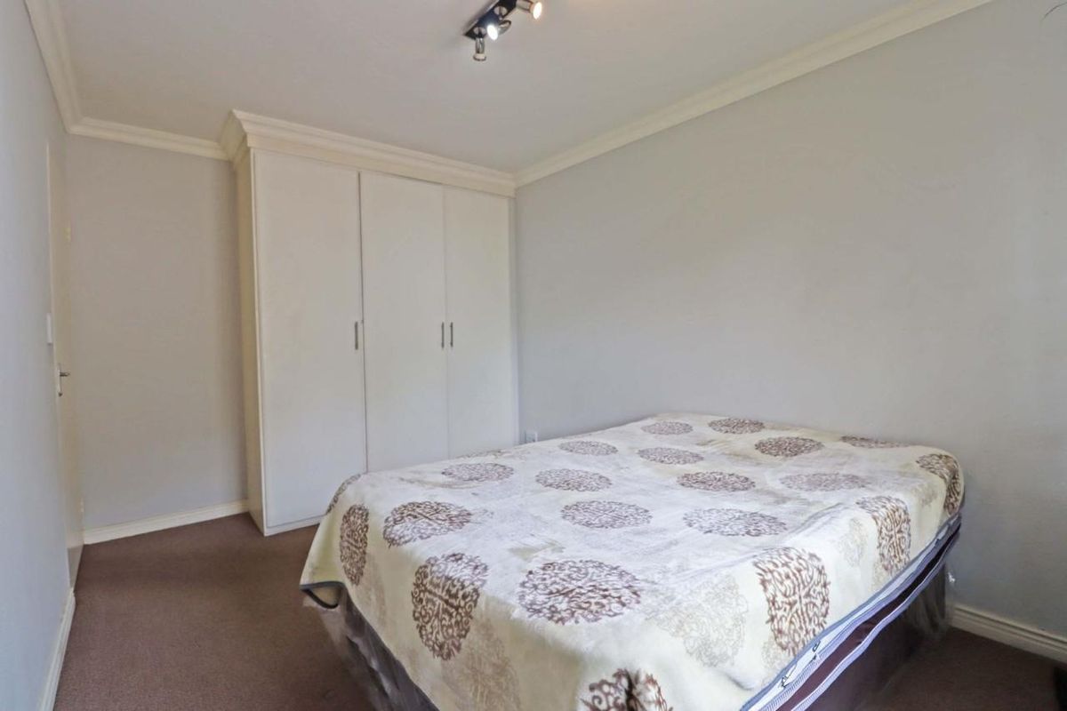 A simple bedroom featuring neutral walls, carpeted flooring, crown molding, and a built-in wardrobe for storage.