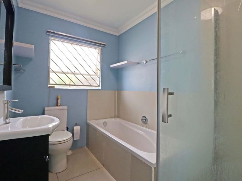 A functional bathroom featuring a built-in bathtub, separate glass shower enclosure, vanity basin, and toilet with tiled finishes.