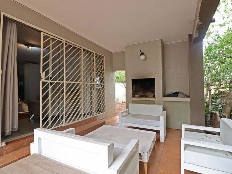 Covered patio featuring a built-in braai, tiled flooring, and direct access to the interior through a security gate and sliding door.
