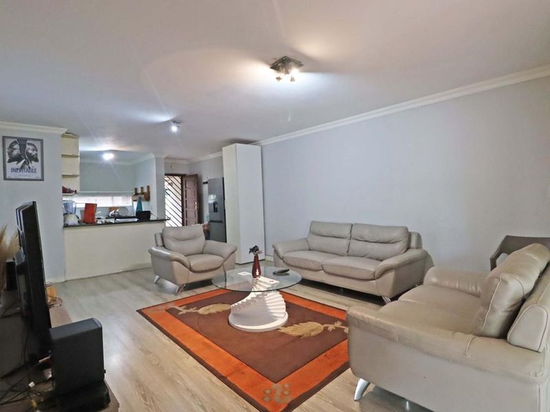 An open-plan living area featuring laminate flooring, cove cornicing, and a functional kitchen with a breakfast bar, offering a versatile layout for modern living.