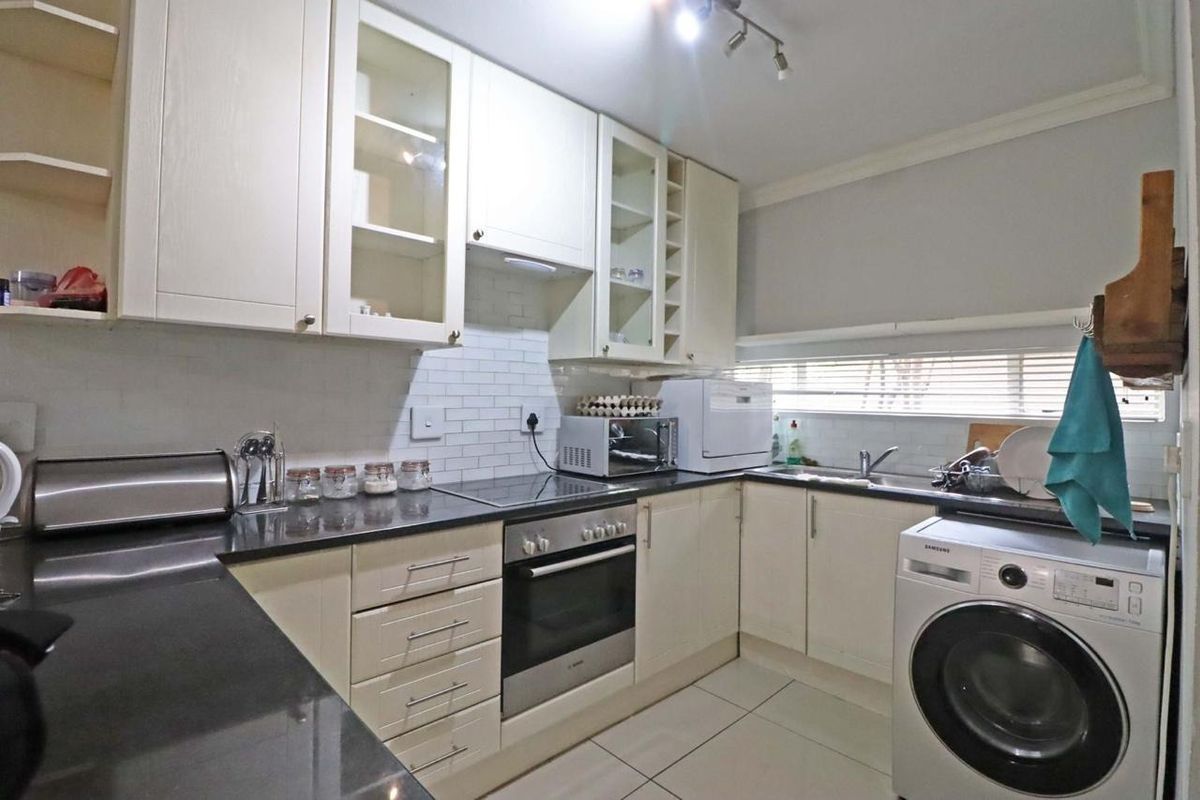 A functional kitchen featuring cream cabinetry, dark stone countertops, subway tile backsplash, and integrated appliances including an oven and cooktop.