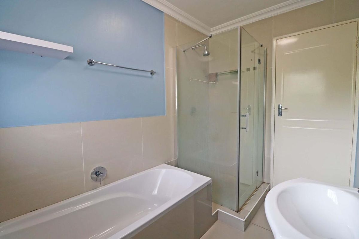 A clean, functional bathroom featuring a built-in bathtub, a separate glass-enclosed shower, and neutral wall tiling with a blue accent wall.