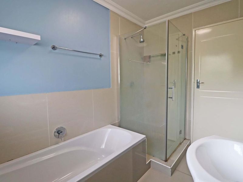 A clean, functional bathroom featuring a built-in bathtub, a separate glass-enclosed shower, and neutral wall tiling with a blue accent wall.