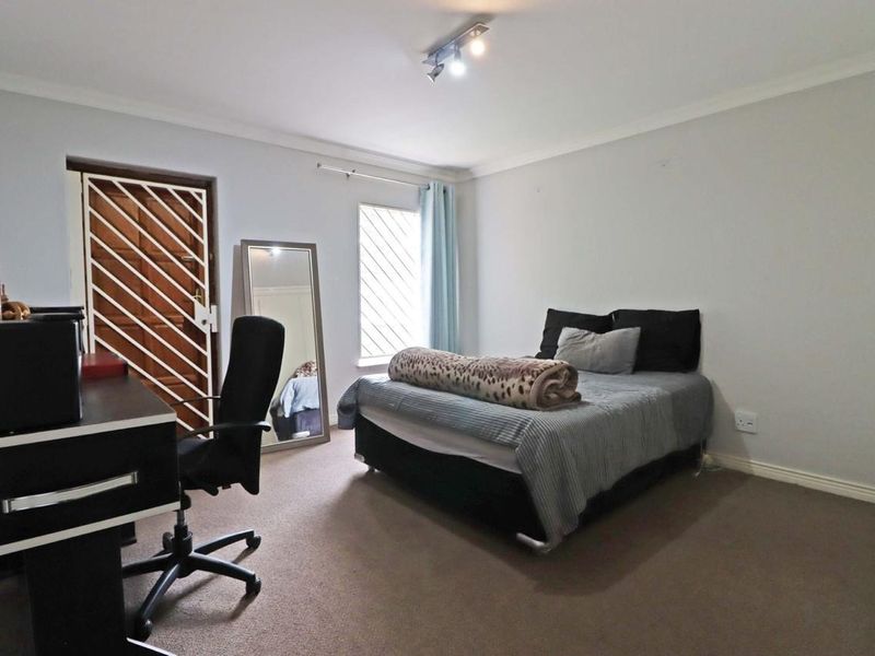 A functional bedroom featuring carpeted flooring, track lighting, and a security gate on the door, providing a neutral base for personalization.