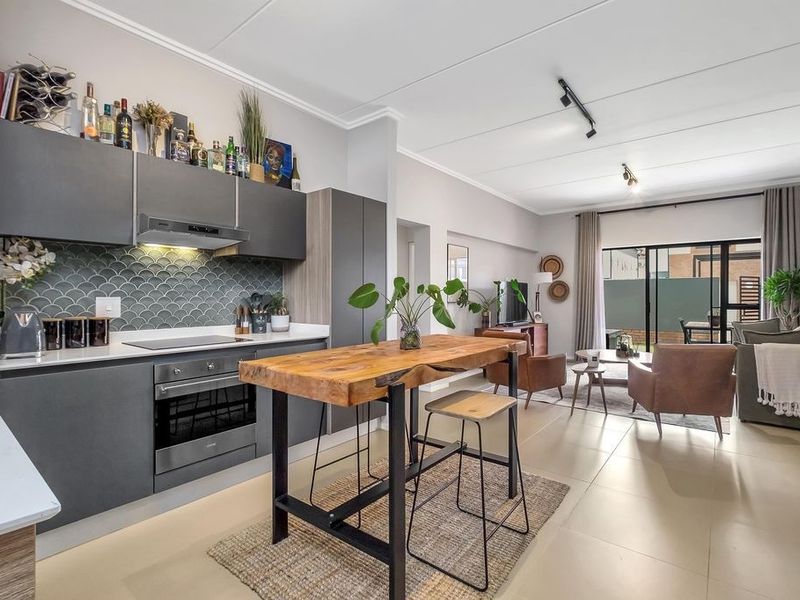 Modern open-plan living area featuring a sleek kitchen with built-in appliances, tiled flooring, and seamless access to an outdoor patio through sliding glass doors.