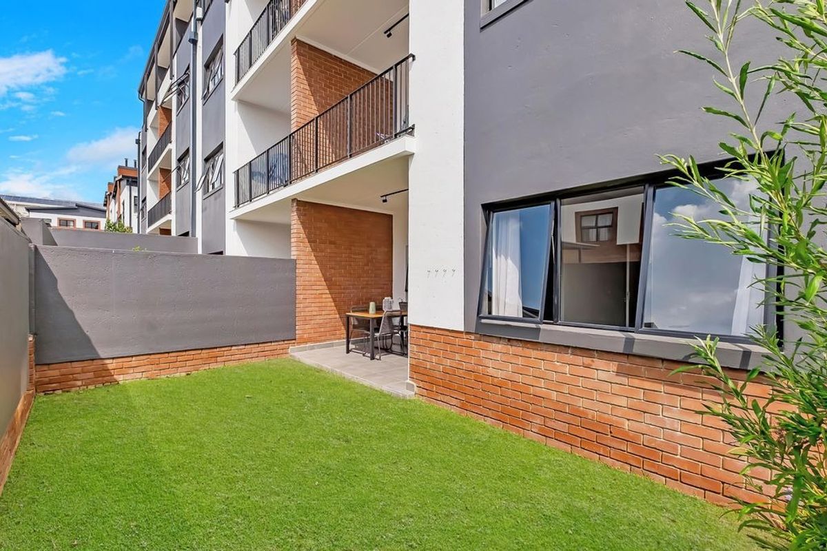 Ground floor apartment exterior featuring a private garden, paved patio area, and access to a balcony with modern brick and render finishes.