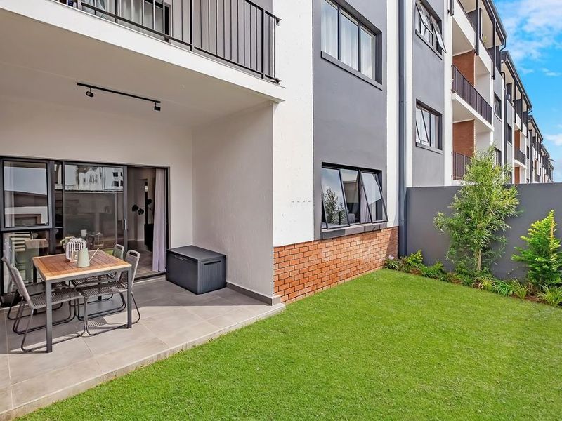 A modern ground-floor apartment featuring a tiled patio area, sliding glass doors, and a private garden with a boundary wall.