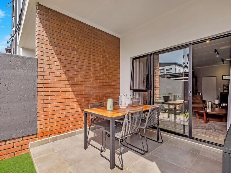 A covered patio area featuring tiled flooring, an exposed brick feature wall, and large sliding glass doors providing access to the interior living space.