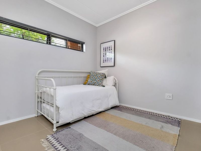 A bright bedroom featuring neutral tiled flooring, a horizontal window, and a built-in cupboard, offering a clean and functional living space.