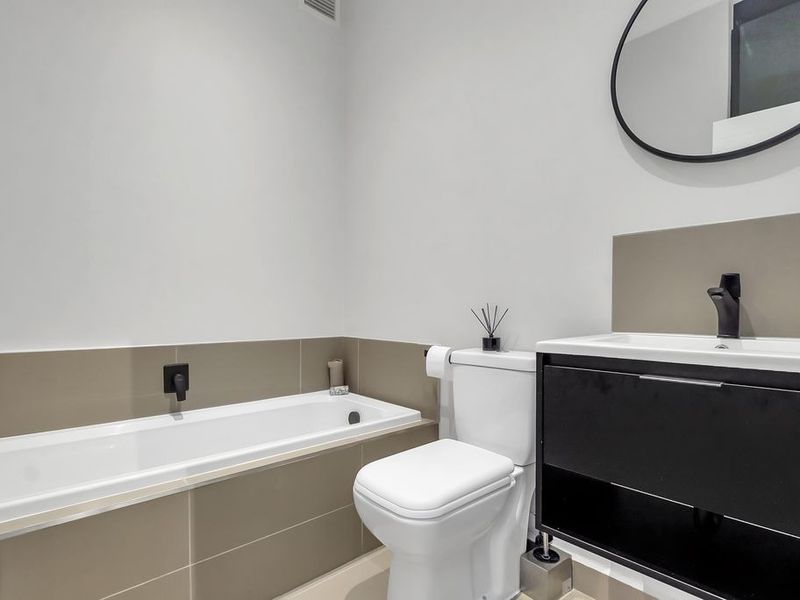Modern bathroom featuring a built-in bathtub, sleek vanity with basin, and contemporary black fixtures with neutral wall tiling.