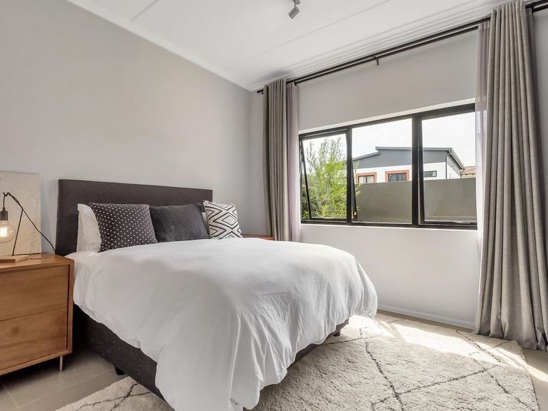 A well-lit bedroom featuring large windows with curtain tracks, neutral wall finishes, and tiled flooring.