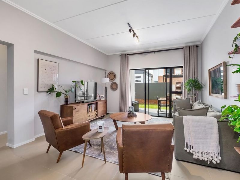 A bright and modern living room featuring tiled floors, track lighting, and a large sliding glass door providing access to the outdoor patio area.