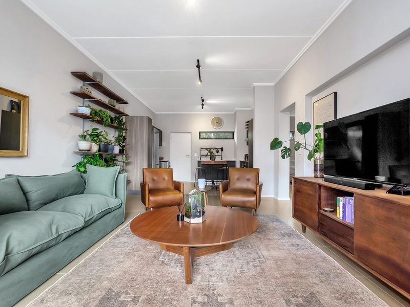A bright open-plan living area featuring modern track lighting, neutral wall finishes, and tiled flooring, seamlessly connecting to the kitchen space.