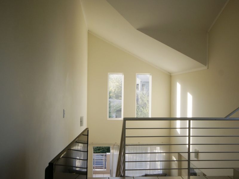 A bright, open-plan hallway featuring a vaulted ceiling, modern metal balustrade, and tall vertical windows that allow for ample natural light.