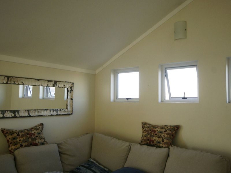 A living area featuring a sloped ceiling, multiple casement windows, and a wall-mounted light fixture.