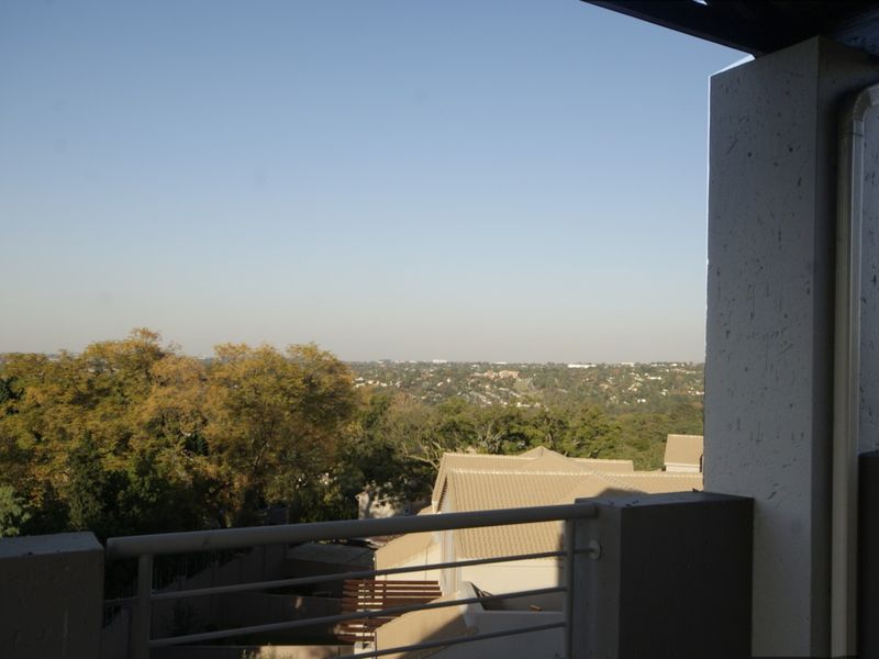 A balcony featuring a metal railing and concrete pillar, offering an expansive elevated view of the surrounding neighborhood and landscape.