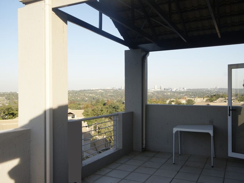 A spacious covered balcony featuring tiled flooring, metal railings, and expansive elevated views of the surrounding landscape and city skyline.